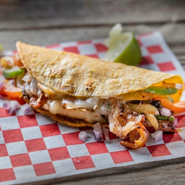 A cheesy quesadilla filled with meat, onions, and peppers, served on red and white checkered paper.