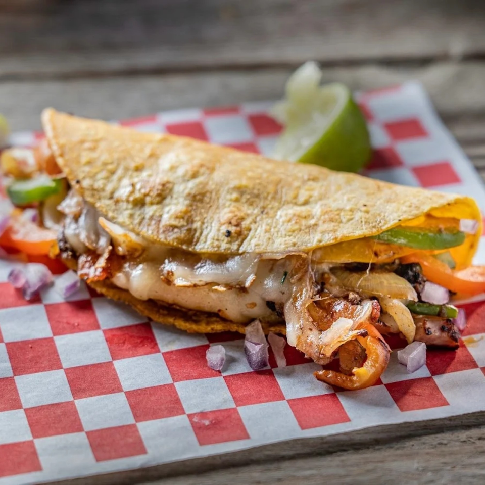 A cheesy quesadilla filled with meat, onions, and peppers, served on red and white checkered paper.