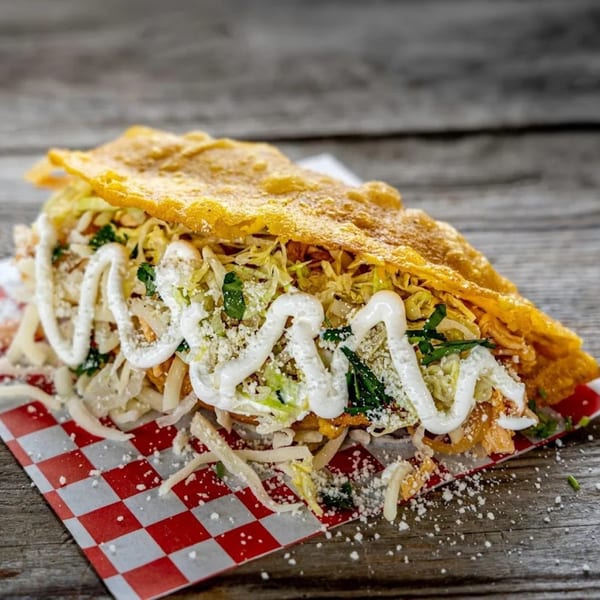A golden-fried taco, generously filled with meat, shredded lettuce, cheese, and drizzled with cream.