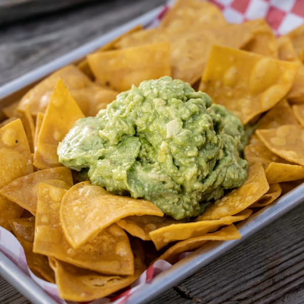 A metal tray filled with golden tortilla chips and a large scoop of guacamole in the center.