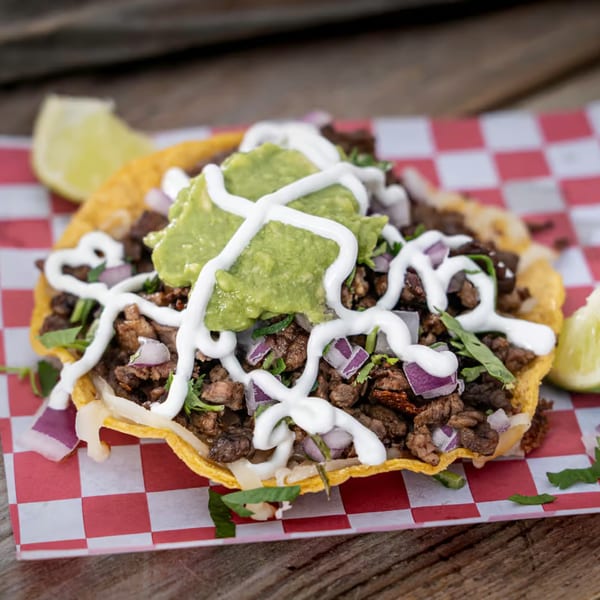 A Tacos El Patron tostada with carne asada, guacamole, sour cream, and red onions.