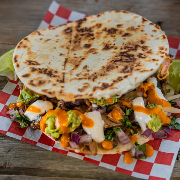A Tacos El Patron Mexican taco with grilled meat, guacamole, sour cream, and orange sauce.