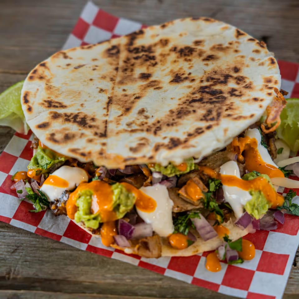 A Tacos El Patron Mexican taco with grilled meat, guacamole, sour cream, and orange sauce.