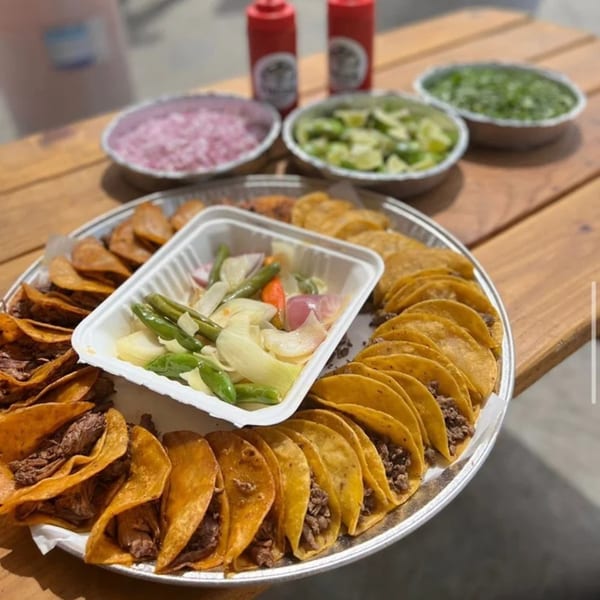 A large platter of tacos, with bowls of toppings and sauces on a wooden table.