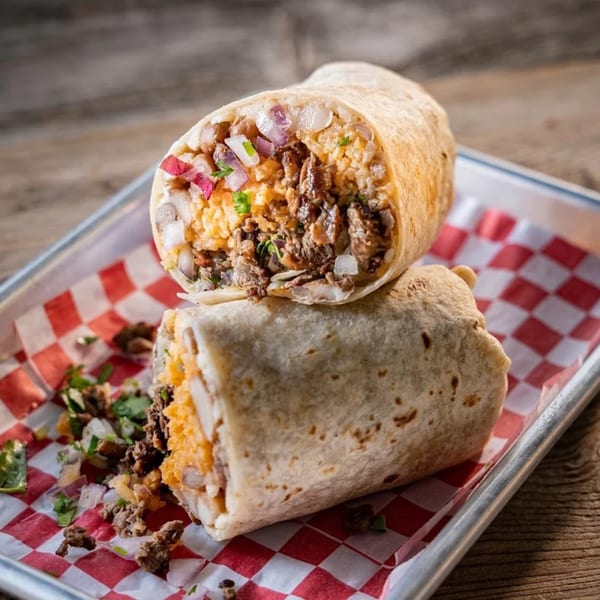 Two large burritos, one cut in half, revealing meat, rice, and red onion on a checkered tray.